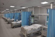 Widok na rząd szpitalnych łóżek, które oddzielają od siebie niebieskie parawany. 