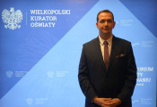 Igor Bykowski, stoi na tle ścianki z napisem Wielkopolski Kurator Oświaty
