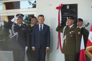 Minister Mariusz Błaszczak w asyście wojskowych odsłania tablicę upamiętniającą por. Łukasza Kurowskiego