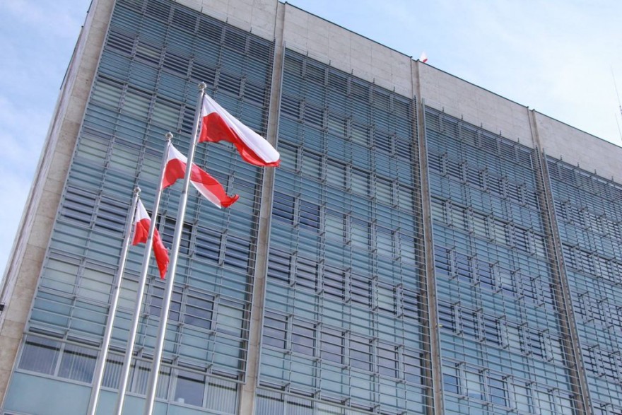 Budynek urzędu na tle trzech flag biało-czerwonych.