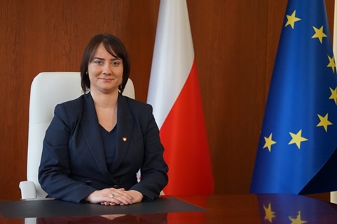 II wicewojewoda wielkopolska Karolina Fabiś-Szulc przy biurku, w tle flagi polska i UE