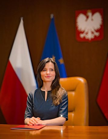Wojewoda wielkopolska Agata Sobczyk przy biurku, z tyłu orzeł polski i flagi polska i UE